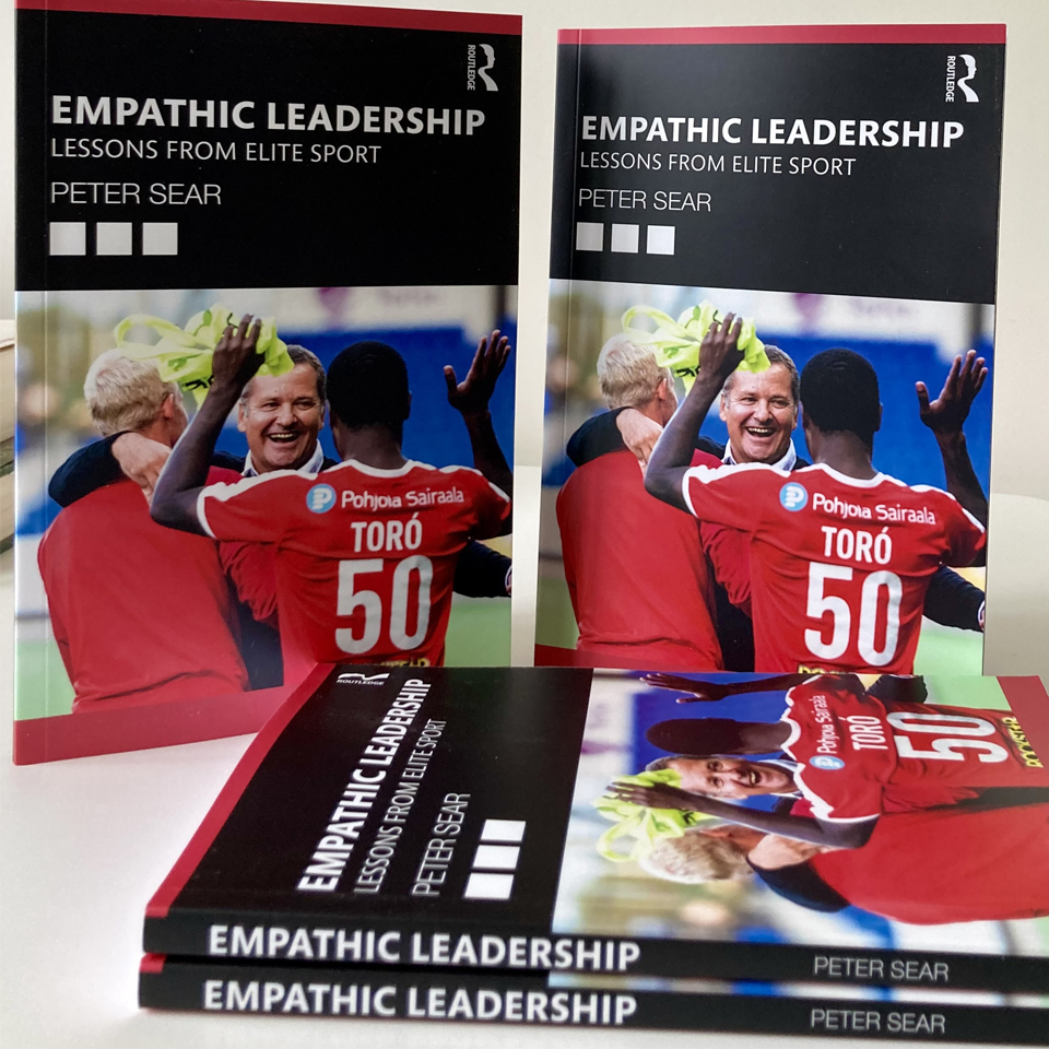 Four of Peter Sear's book displayed. the book cover is black and red with the image of two footballers in red kit hugging a man dressed in a suit and celebrating. The text reads'Empathetic Leadership: Lessons from Elite Sport' 'Peter Sear' 